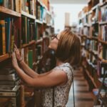 woman standing between library book shelves