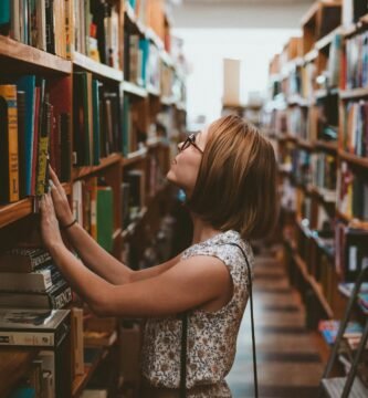 woman standing between library book shelves